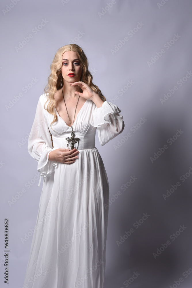 Close up portrait of beautiful blonde model wearing elegant white halloween gown, a historical fantasy character. Holding crucifix cross necklace, isolated on studio background. Close up portrait of beautiful blonde model wearing elegant white halloween gown, a historical fantasy character. Holding crucifix cross necklace, isolated on studio background.