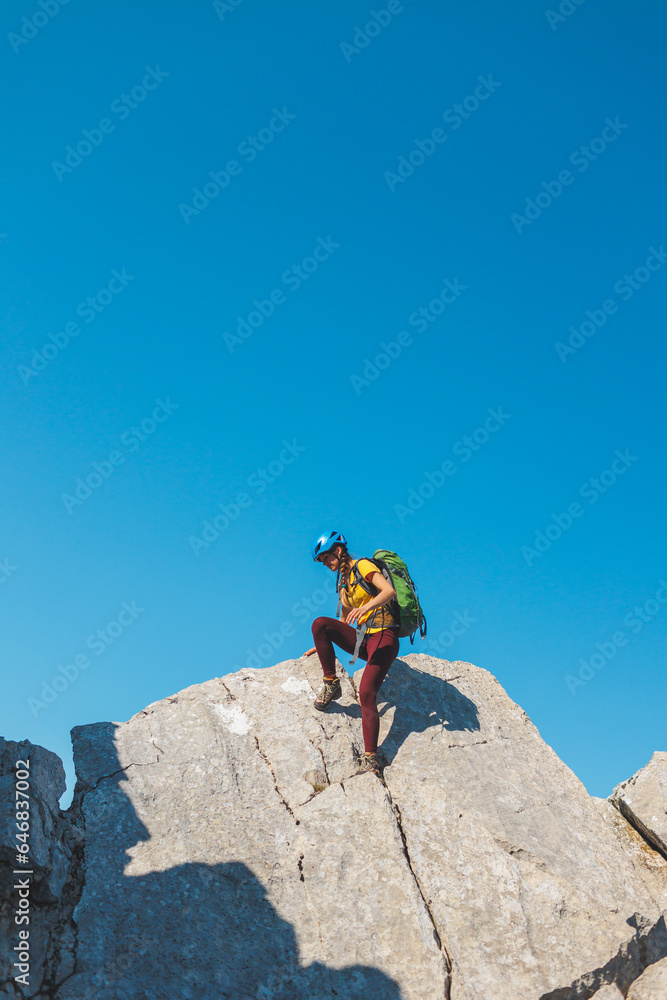The girl is climbing the rock. Woman climber with a backpack and a helmet in the mountains. adventure and mountaineering concept. hiking with a backpack. mountains of Turkey..