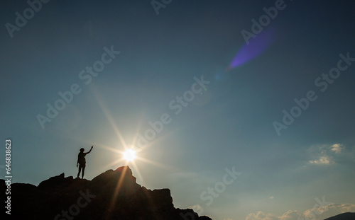 Silhouette of a girl with a backpack on a rock at sunset. The silhouette of the winner on the top of the mountain. The concept of sports and active life.