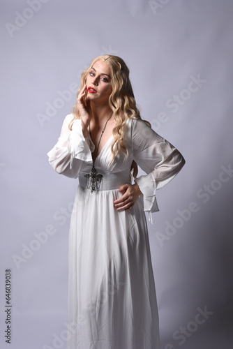 Close up portrait of beautiful blonde model wearing elegant white halloween gown, a historical fantasy character. Holding crucifix cross necklace, isolated on studio background.