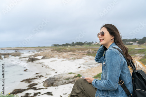 stylish asian Korean woman tourist feeling comfortable with cool sea wind while relaxing at coastal beach along pacific coast highway in California usa