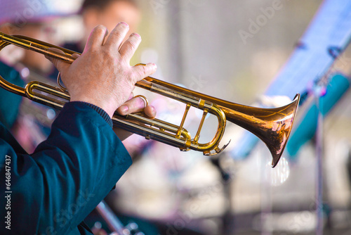 close-up of the hands of a  musician holding a gold-colored pump-action trumpet