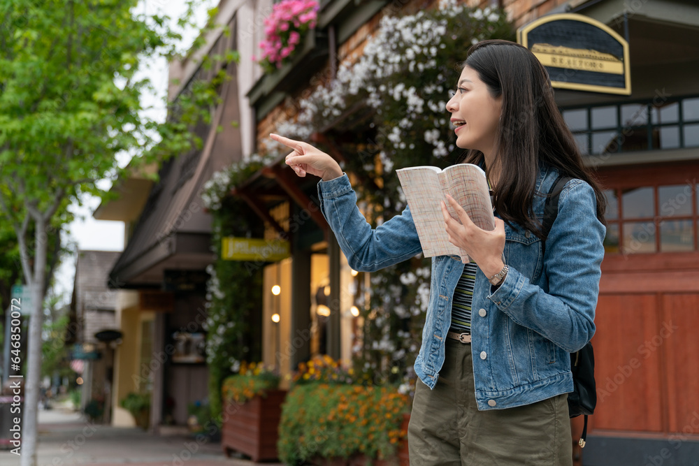 travel lifestyle and people on vacation in usa. cheerful asian female traveler pointing at a landmark in distance with a guidebook in hand on street corner while visiting Carmel by the sea