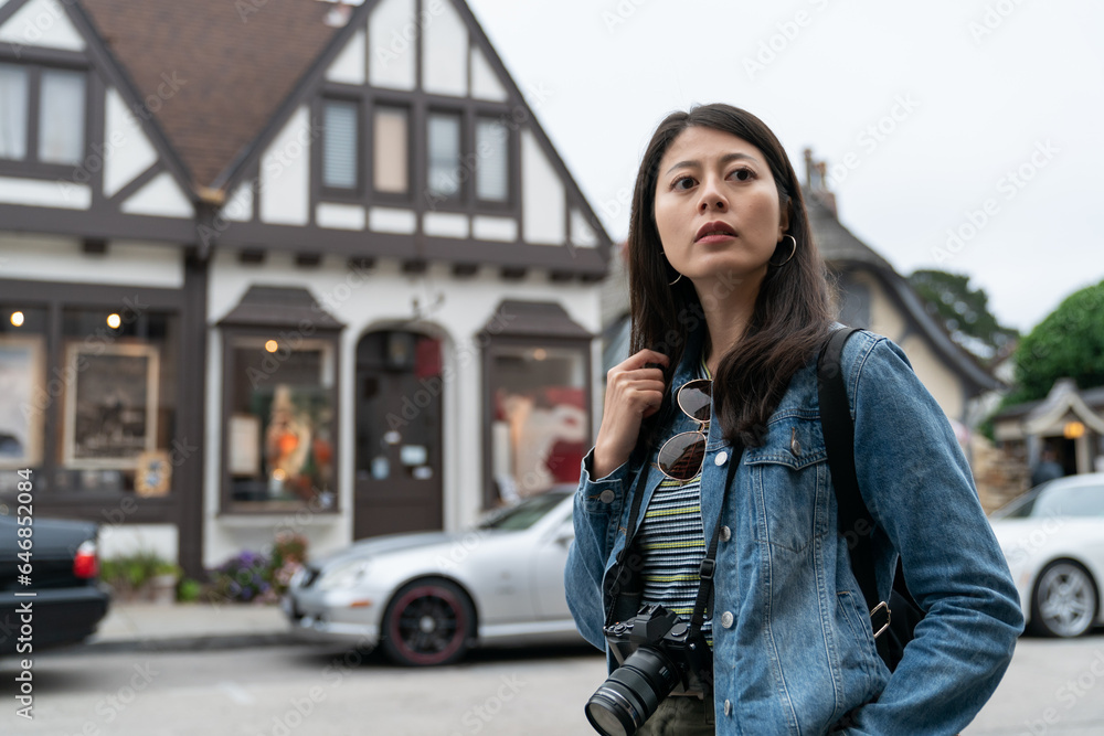 Fototapeta premium asian korean woman photographer looking into distance with curiosity on the street while touring Carmel by the sea in California usa with an European style house at background
