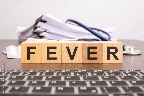 wooden block form the word FEVER with stethoscope, pills, notepad on the doctor's desktop - medical concept