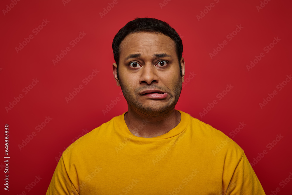 worried indian man in bright clothes looking at camera and grimacing on red background, stroke worried indian man in bright clothes looking at camera and grimacing on red background, stroke