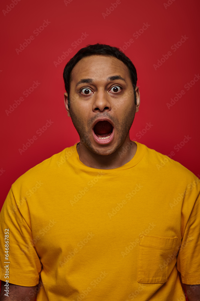 shock expression, indian man in yellow clothes looking at camera with open mouth on red backdrop shock expression, indian man in yellow clothes looking at camera with open mouth on red backdrop