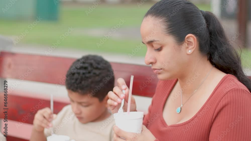 Latin mom having a soft drink with her son, sitting on an outdoor bench Latin mom having a soft drink with her son, sitting on an outdoor bench