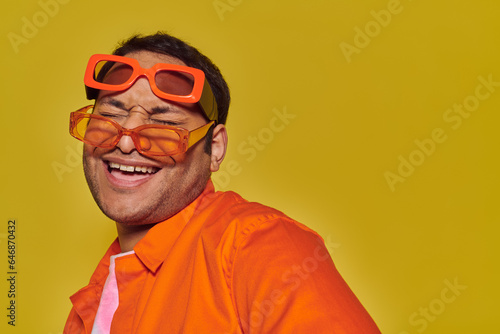 fashionable indian man trying on different trendy sunglasses and smiling on yellow backdrop