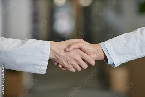 Hands of two clinicians in lab coats welcoming one another while standing in front of camera during greeting or congratulations in hospital