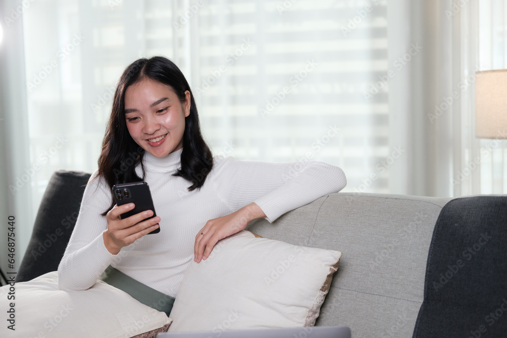 Asian woman enjoys shopping online, chatting with her friends, and reading online blogs while relaxing on a sofa in her living room. Asian woman enjoys shopping online, chatting with her friends, and reading online blogs while relaxing on a sofa in her living room.