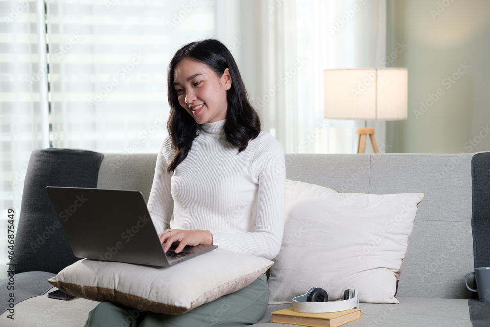 Young business freelance Asian woman working on laptop checking social media while lying on the sofa when relax in living room at home. Young business freelance Asian woman working on laptop checking social media while lying on the sofa when relax in living room at home.