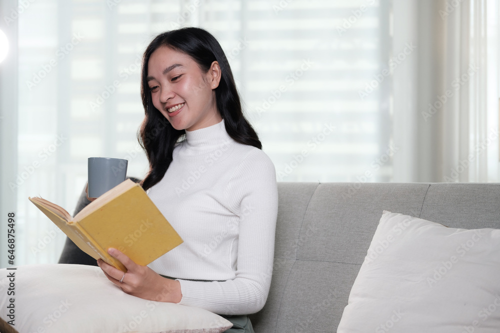 Attractive young Asian woman sits in the minimal and comfortable living room enjoying reading a book. Attractive young Asian woman sits in the minimal and comfortable living room enjoying reading a book.
