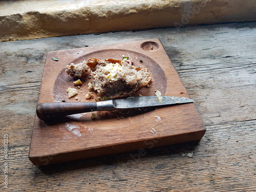 An old square wooden plate with scraps of food and an antique knife resting on it.