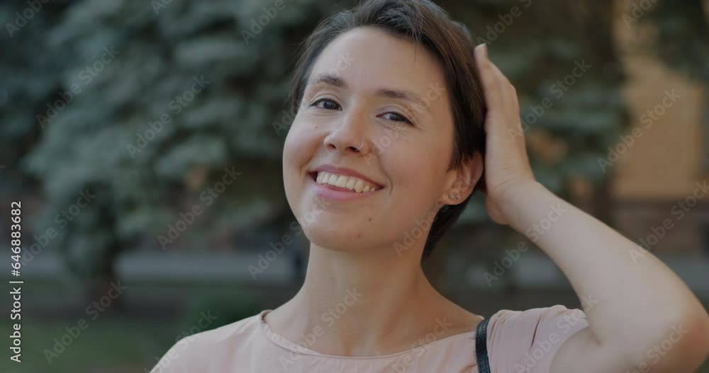 Portrait of charming young woman touching hair and smiling standing outdoors in modern city. Stylish people and millennials concept. Portrait of charming young woman touching hair and smiling standing outdoors in modern city. Stylish people and millennials concept.