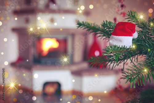 Christmas hat on fir tree branch and blur burning fireplace background.