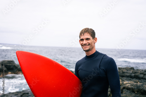 happy surfer in the coast with his red surfboard