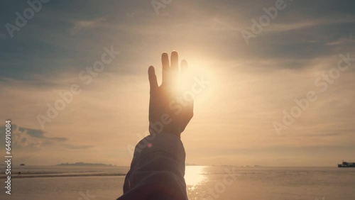 A woman's hand against the background of the summer sky. Close-up of a chewy dreamer stretching out her hand to the sun at sunset. The sun's rays shine through the hand. Summer dreaming concept. photo