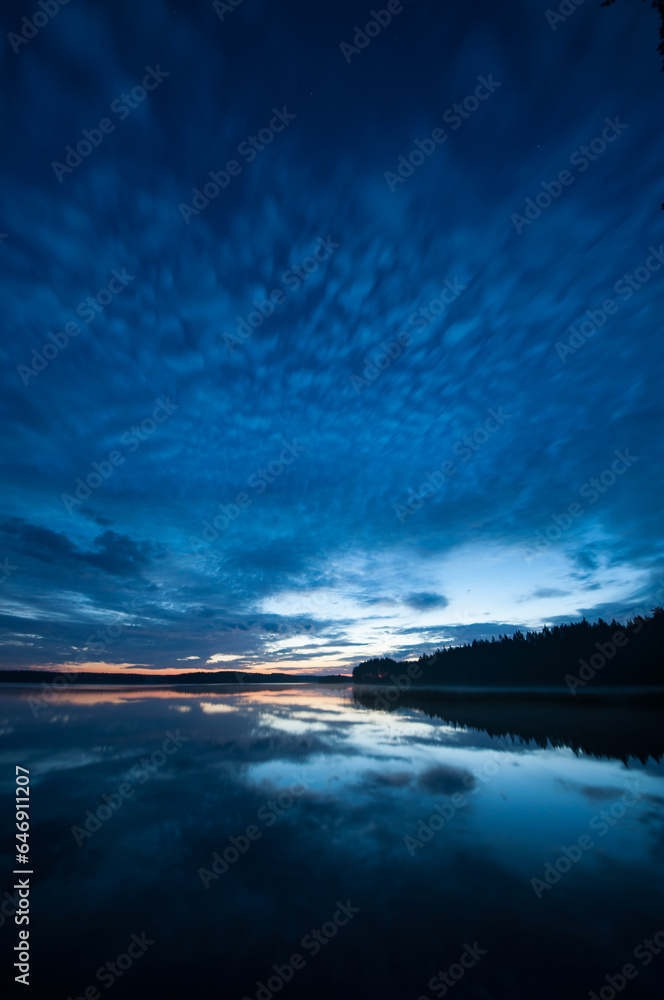 Blue evening colors and cloud formations reflected on the surface of a calm lake in the forests of Finland