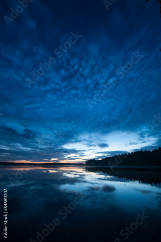 Blue evening colors and cloud formations reflected on the surface of a calm lake in the forests of Finland