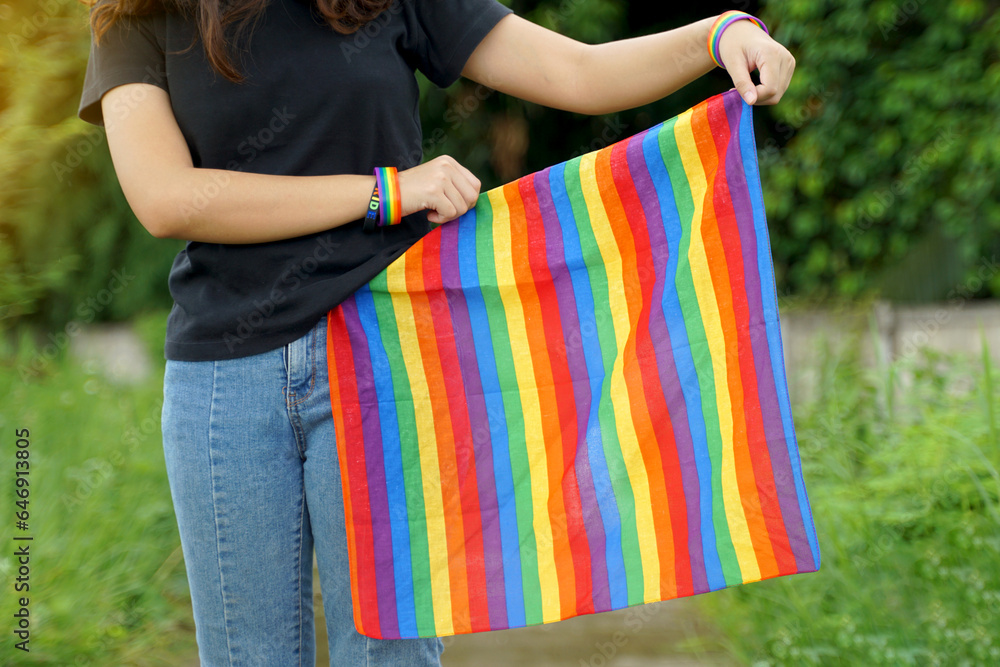 An Asian woman tucks the end of a rainbowcolored striped cloth around the waist of her jeans