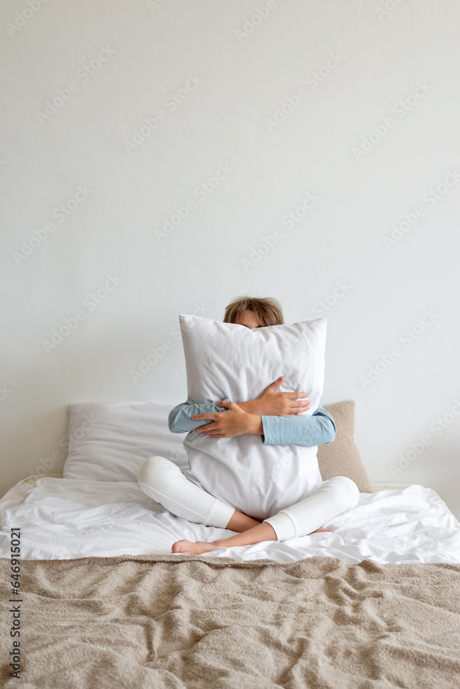 Healthy sleep, dream concept. Teenager boy sitting on bed, embracing pillow, minimalist nordic bedroom interior, lifestyle Healthy sleep, dream concept. Teenager boy sitting on bed, embracing pillow, minimalist nordic bedroom interior, lifestyle