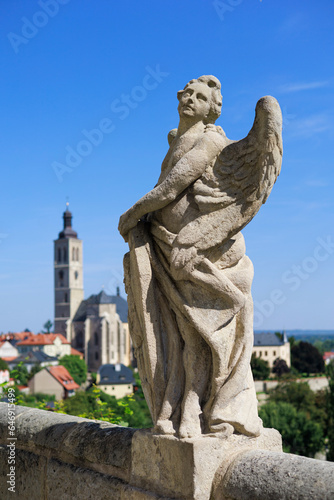 Statue of angel, Kutna Hora, Czech Republic, Czechia - old religious sculpture and church of saint James (Kostel svateho Jakuba) in the background. Sunny and shallow focus. © M-SUR