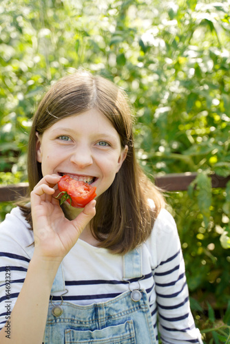 happy girl eats a red tomato in a greenhouse