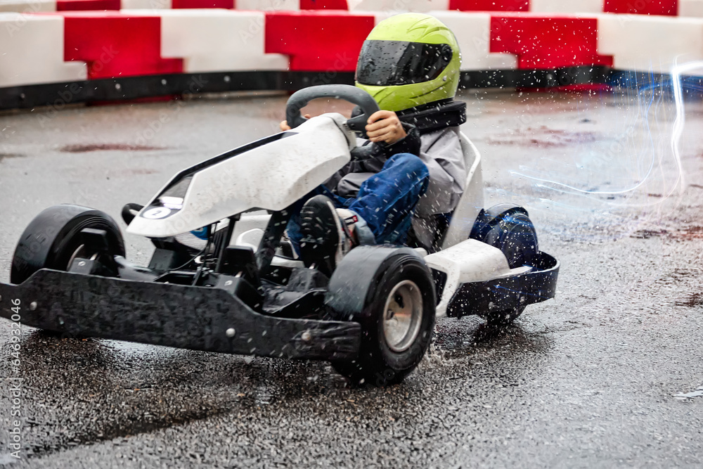 Young boy rides a racing kart on the track on wet asphalt like an adult. Child in a green protective helmet driving a racing car on a kart learns to drive