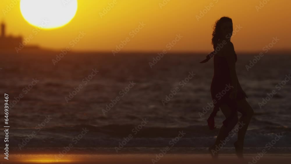Dark silhouette of dancing young woman on the seashore during sunset Dark silhouette of dancing young woman on the seashore during sunset
