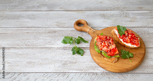 Fototapeta Naklejka Na Ścianę i Meble -  Bruschetta with cottage cheese, avocado, tomatoes, greens, white sesame seeds. Healthy food, rich in healthy fats, fiber, vitamins, antioxidants. Vegetarian food.