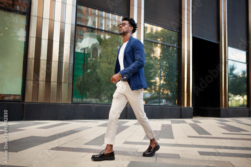 Side view full length man walks outside and wears trendy business clothes, blue jacket, white pants and loafer shoes. Stylish male fashion model, Street style