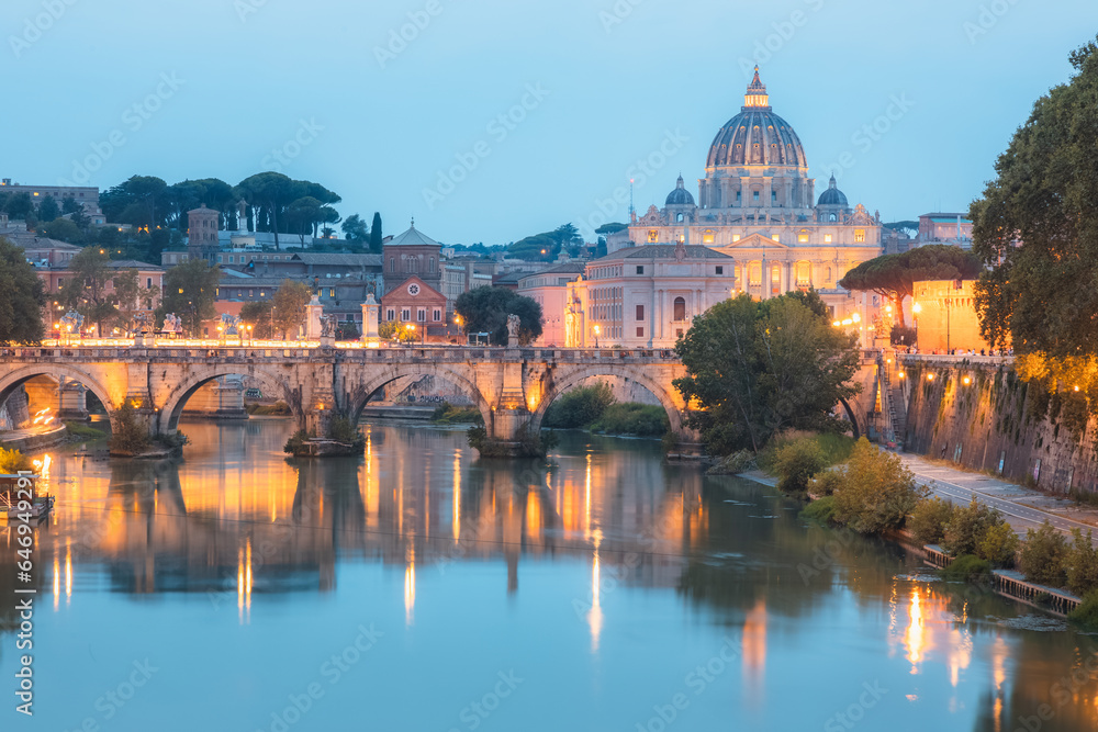 Fototapeta premium Sceninc twilight view of Saint Peter's Basilica at Vatican City and Ponte Vittorio Emanuele II illuminated along the Tiber River on a summer evening in Rome, Italy.
