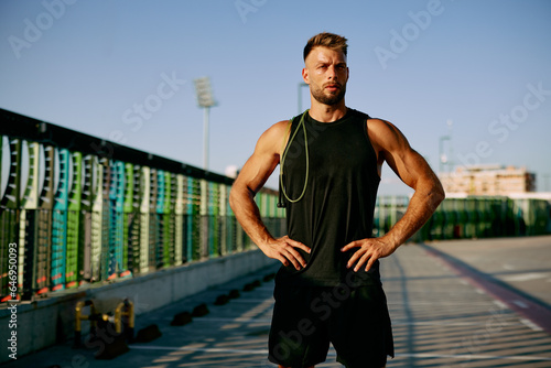 Handsome sports man posing with jump rope on his shoulder after training in black sports clothes