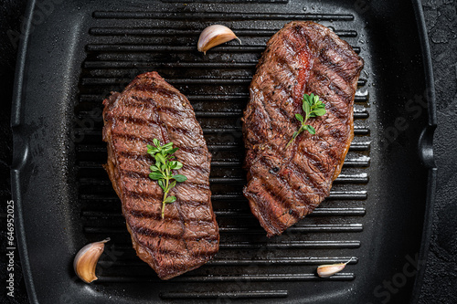 Grilled Top Blade or flat iron roast beef meat steaks on a skillet. Black background. Top View