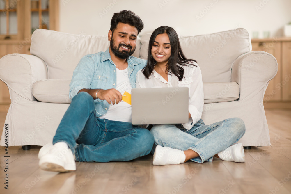 Happy hindu couple shopping online with laptop and credit card from home, sitting on floor in living room, free space Happy hindu couple shopping online with laptop and credit card from home, sitting on floor in living room, free space