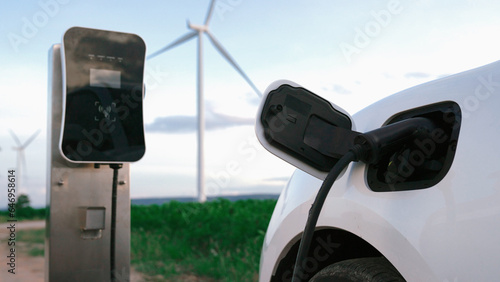 Progressive future energy infrastructure concept of electric vehicle being charged at charging station powered by green and renewable energy from a wind turbine in order to preserve the environment.