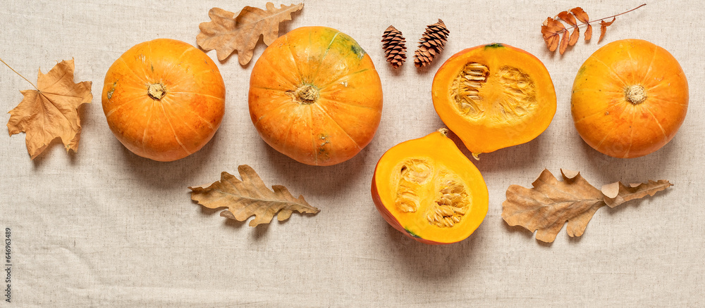 Fresh pumpkins with autumn leaves on a beige textile background. Top view, flat lay, banner.