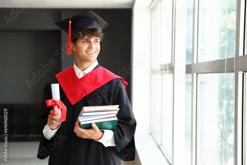Male graduate student with diploma and books near window in room