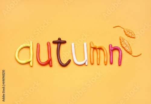 Word AUTUMN made of play dough on orange background