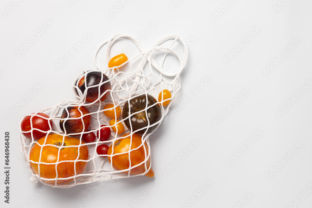 Multicolored yellow, black, red tomatoes in a white mesh shopping bag on a white background, top view