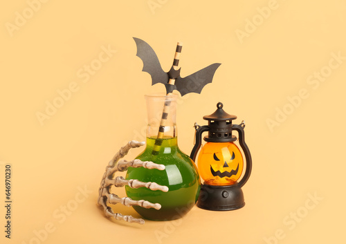 Test tube of delicious green cocktail for Halloween with skeleton hand and lantern on beige background