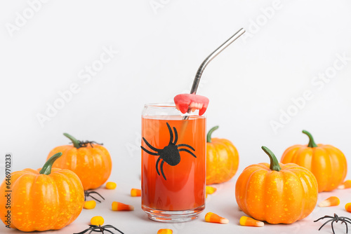 Glass of delicious cocktail for Halloween with candy corns and pumpkins on light background, closeup