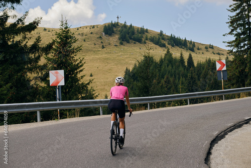 Back view of a female cyclist during a ride. Woman cyclist is wearing cycling kit and a helmet while riding her gravel bicycle through stunning Romanian mountain landscapes. Bucegi Mountains photo