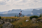 Professional male cyclist is riding a gravel bike on a gravel road with an amazing view of the mountains. Cyclist is practicing on gravel road. Man is riding on top of a hill.Bucegi Mountains, Romania