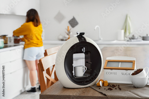 Modern coffee machine with cups, roasted beans and pods on table in kitchen