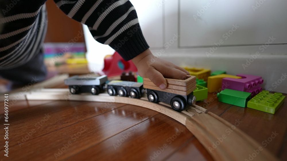 Little boy playing with vintage wooden train tracks, child immersed in imaginative play pushing retro wagon with hand
