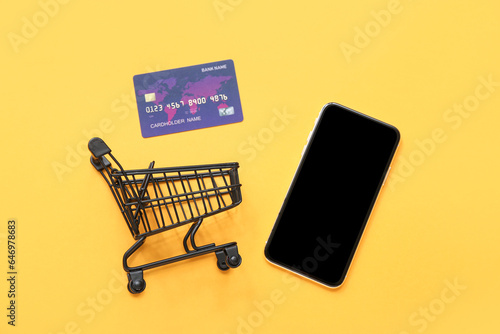 Small shopping cart, credit card and mobile phone on yellow background