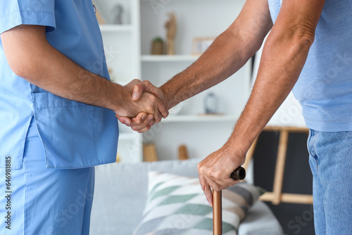 Male nurse with senior man shaking hands at home, closeup