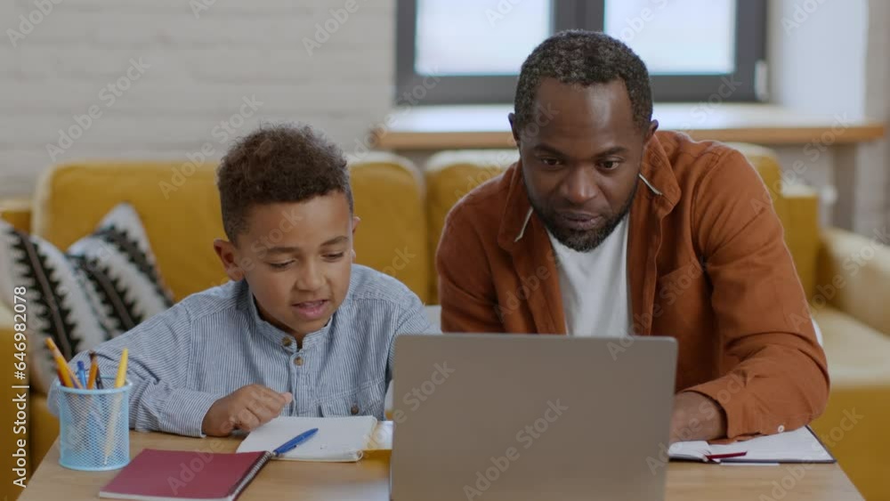 Cute little black boy studying online at home with his daddy, enjoying well done homework, tracking shot, slow motion Cute little black boy studying online at home with his daddy, enjoying well done homework, tracking shot, slow motion